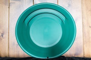 A green plastic gold panning pan from a Gold Panning Kit sits on a wooden surface, viewed from above.