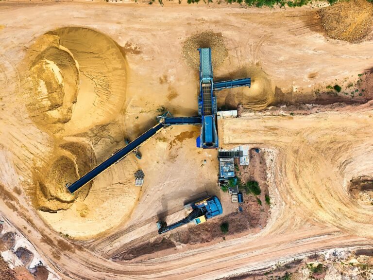 Aerial view of an industrial sand mining operation highlights large yellow sand piles, conveyor belts, and heavy machinery—a modern scene reminiscent of the geological journey of gold.
