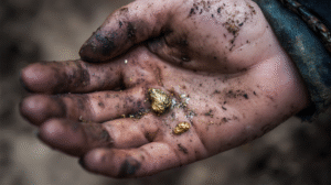 A dirty hand holding small gold nuggets and specks of dirt, showcasing unique Gold Nugget Characteristics.