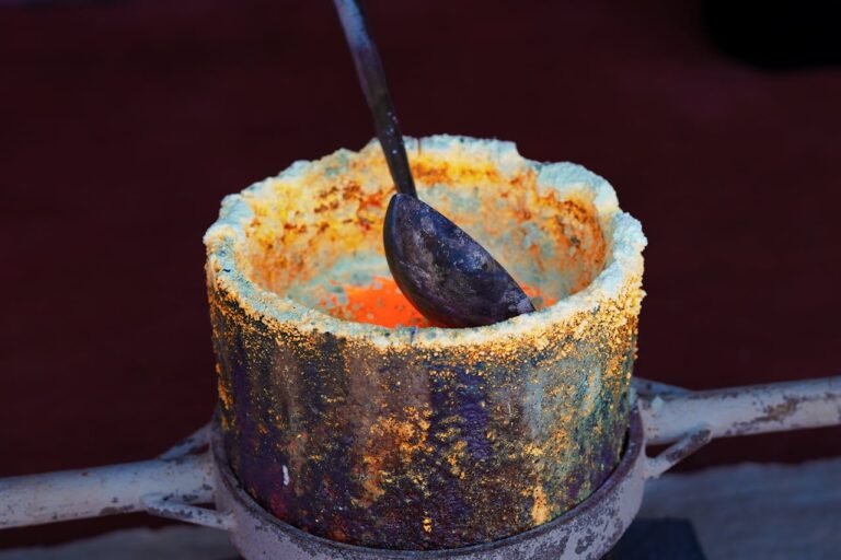 A close-up of a metal crucible containing molten material showcases gold refining and extraction methods, with a metal ladle resting inside. The crucible’s rim displays oxidation and mineral buildup.
