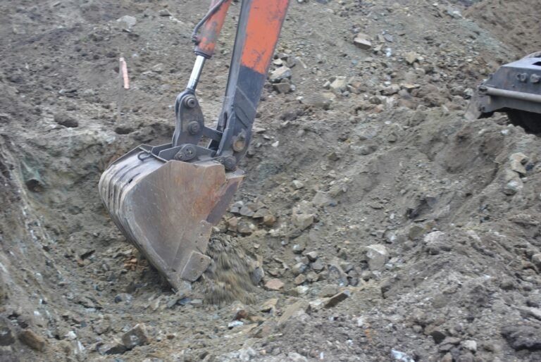 Handling Difficult Ground Conditions A close-up of an excavator bucket digging and lifting soil and rocks at a construction site, expertly handling difficult ground conditions.