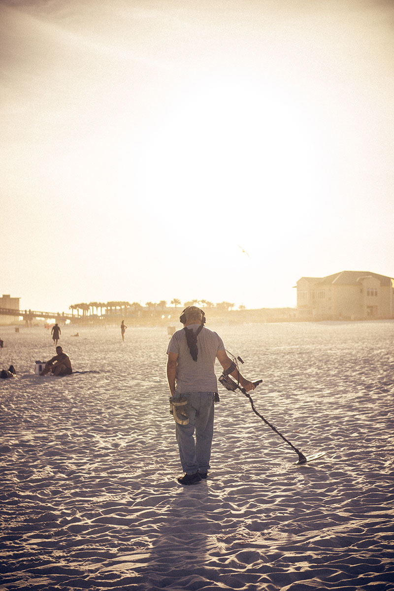 A man walks on the sandy beach, holding a kite in his hand.